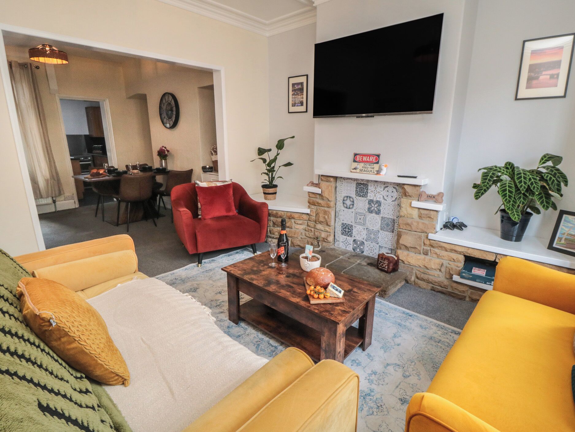 A living room with a sofa, armchair, coffee table, fireplace, TV, and dining area.