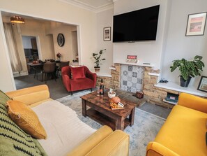 A living room with a sofa, armchair, coffee table, fireplace, TV, and dining area. - Captain Jacks (Whitby)