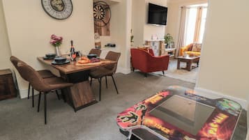 A dining area with a wooden table, chairs, a dartboard, and a clock on the wall.
