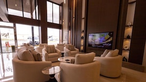 Een ruime woonkamer met meerdere banken en een salontafel, een aan de muur bevestigde televisie en grote ramen voor natuurlijk licht.