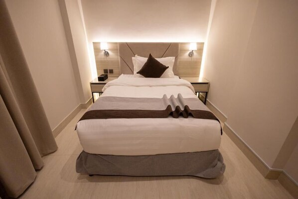 Una habitación de hotel con una cama grande, dos mesitas de noche y un cabecero con iluminación integrada.