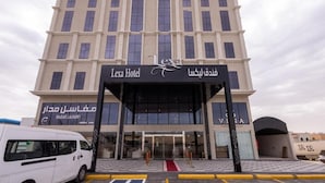 Een hotelingang met een hellingbaan, een witte bestelwagen geparkeerd ervoor, en een bord met 'Lexa Hotel' in zowel Engels als Arabisch.