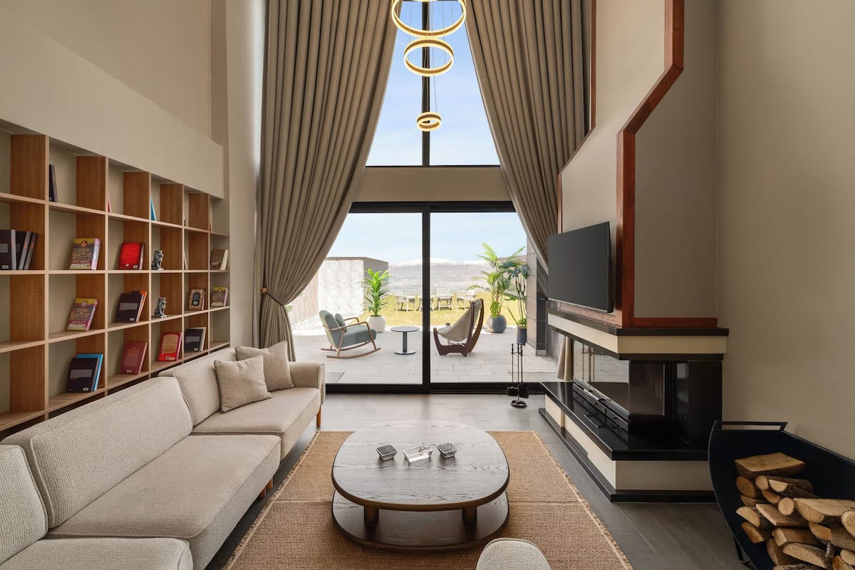 Ein modernes Wohnzimmer mit Sofa, Couchtisch, Bücherregal, Fernseher, Kamin und Blick durch eine Glastür.