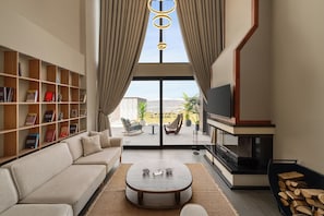 A modern living room with a sofa, coffee table, bookshelf, TV, fireplace, and a view through a glass door.