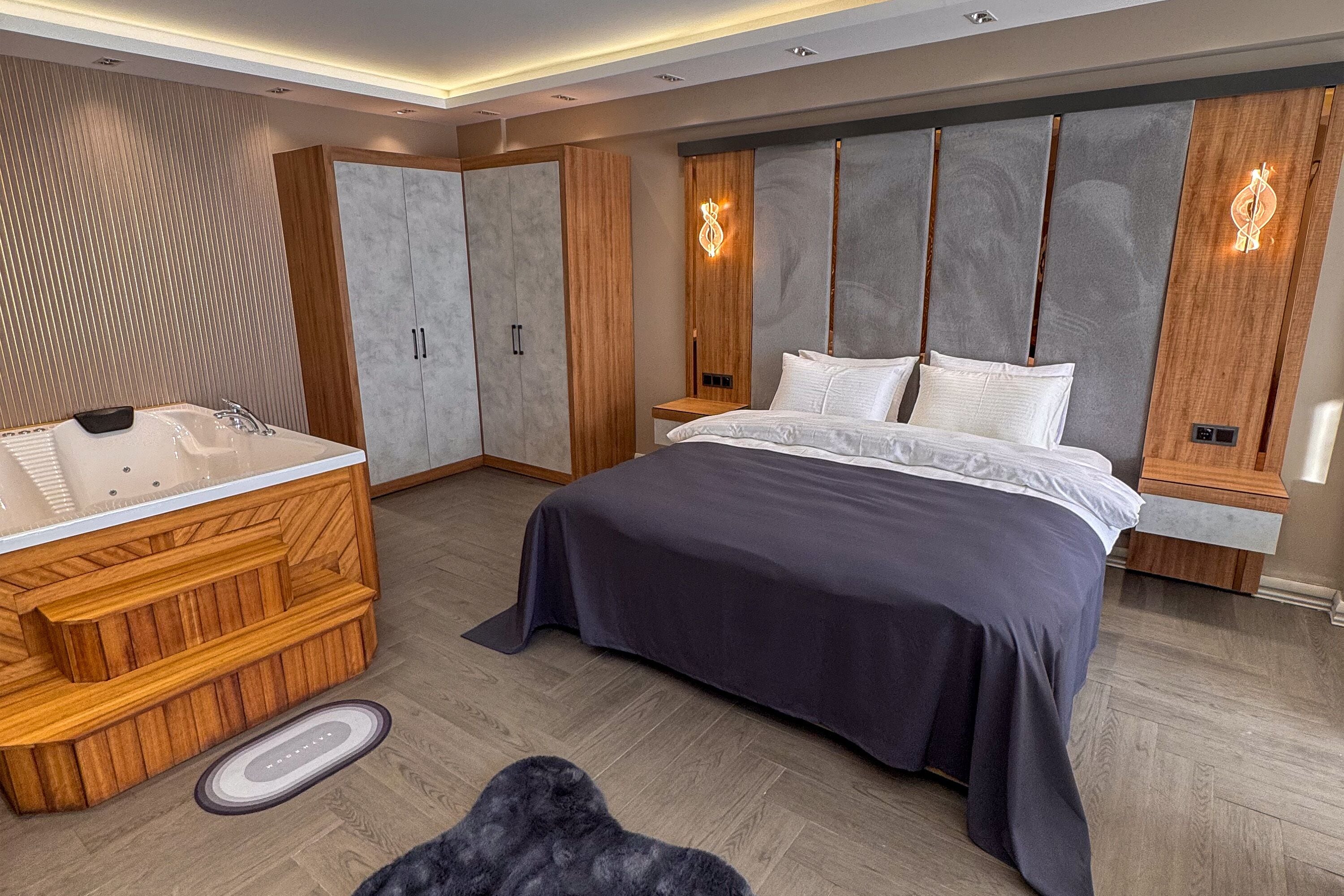 A modern bedroom with a large bed, a wooden vanity with a bathtub, and built-in wardrobes.