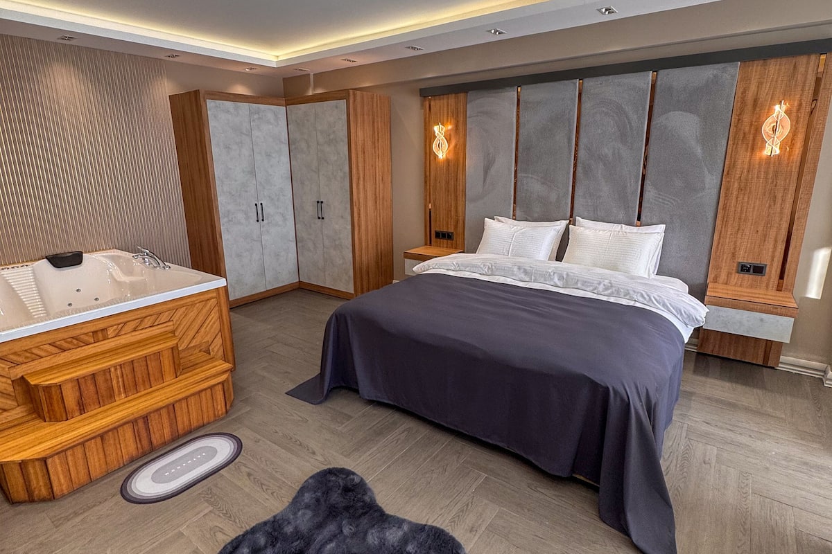 A modern bedroom with a large bed, a wooden vanity with a bathtub, and built-in wardrobes.