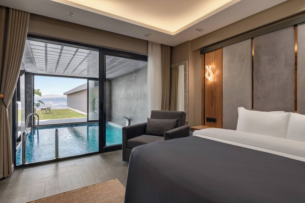Ein modernes Hotelzimmer mit einem großen Bett, einer Sitzecke, Blick auf einen Pool und einem Balkon.