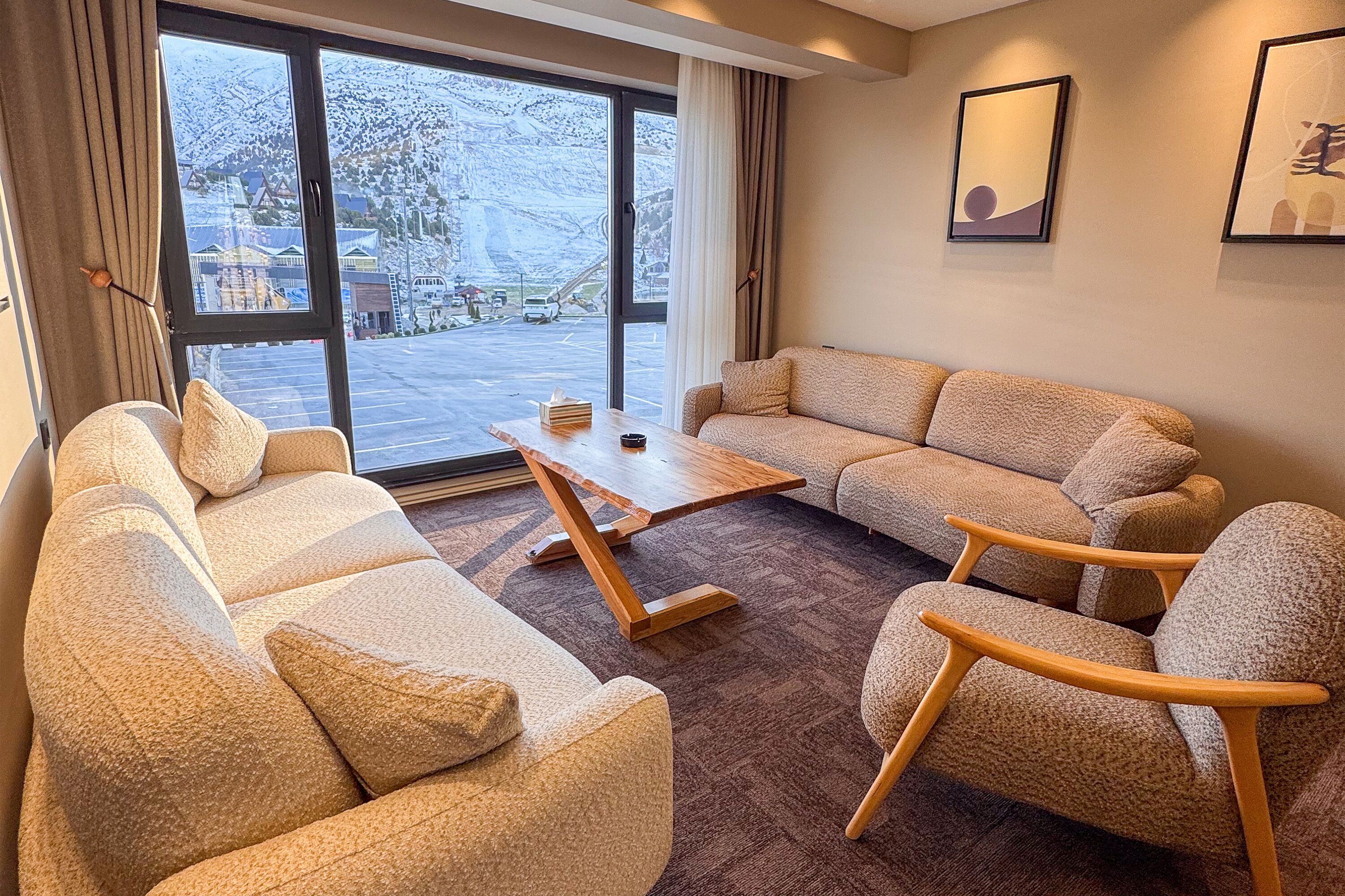 Una sala de estar con sofá, sillón y mesa de centro, ventanas amplias con vista a un paisaje nevado y obras de arte enmarcadas en la pared.