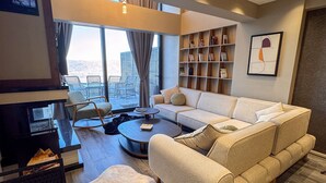 A modern living room with a sofa, coffee table, and a fireplace. There is a balcony with outdoor furniture and a bookshelf with framed items. - Ramada by Wyndham Erzincan Ergan (Erzincan)