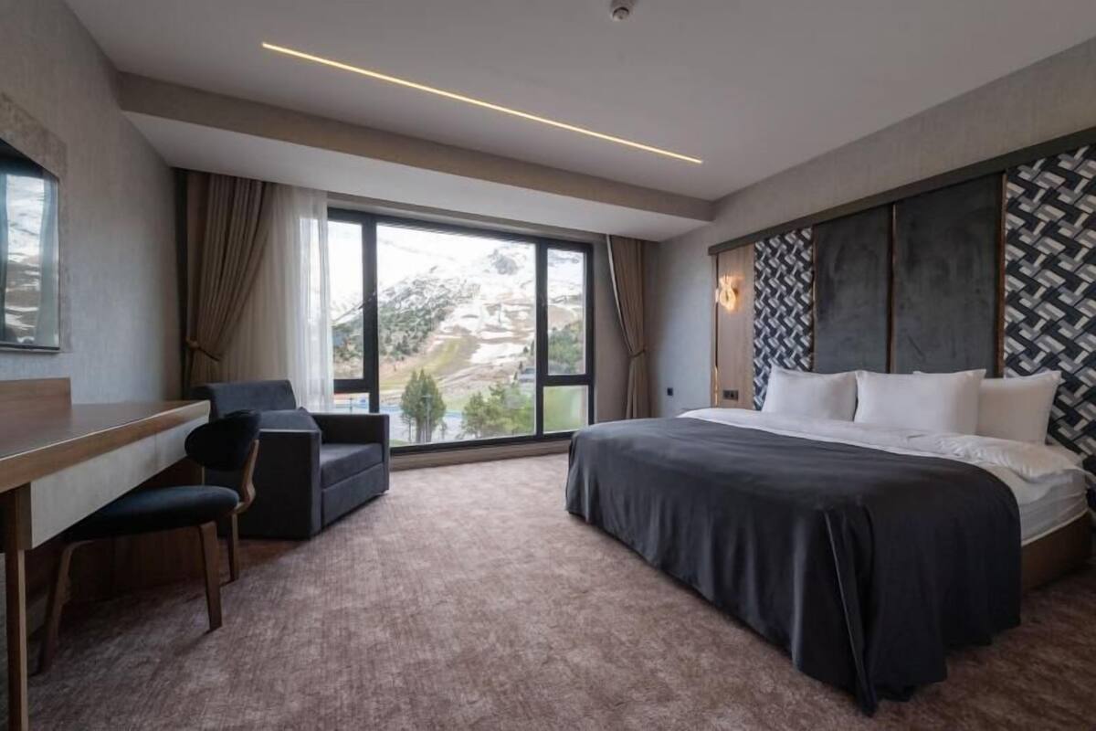 Ein Hotelzimmer mit einem Bett, einem Schreibtisch, einem Sessel und einem großen Fenster.