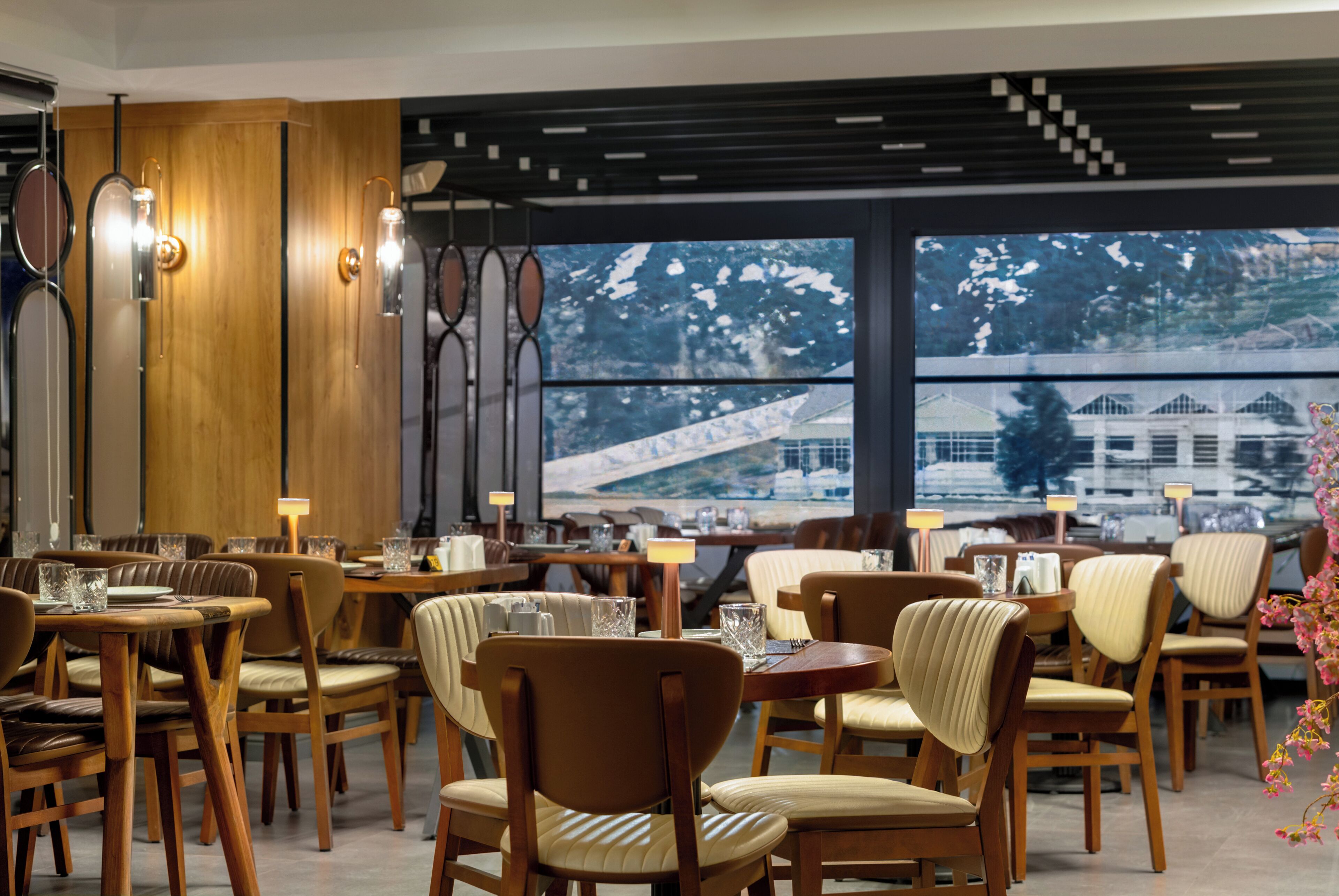 A restaurant with wooden furniture, pendant lighting, and large windows with a view of snow-covered buildings.