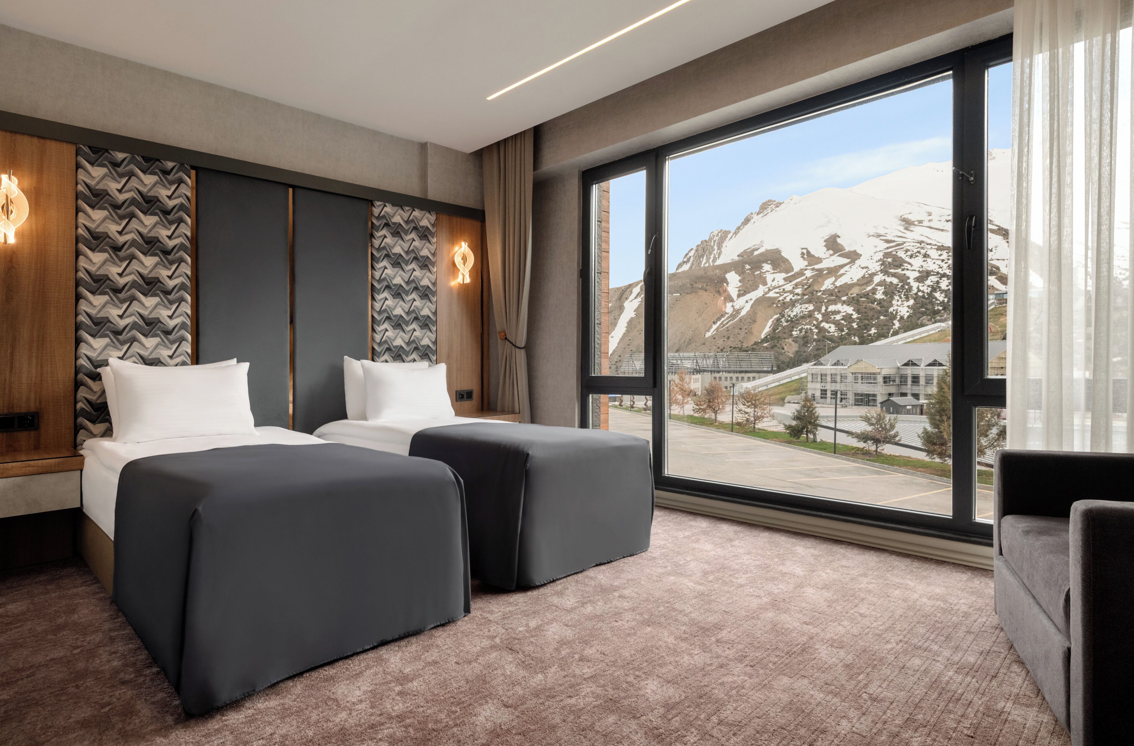 A hotel room with two beds, a large window with a mountain view, and a modern interior design.