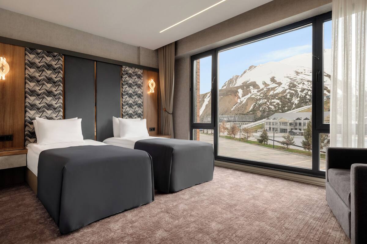 Ein Hotelzimmer mit zwei Betten, einem großen Fenster mit Bergblick und einem modernen Interieur.