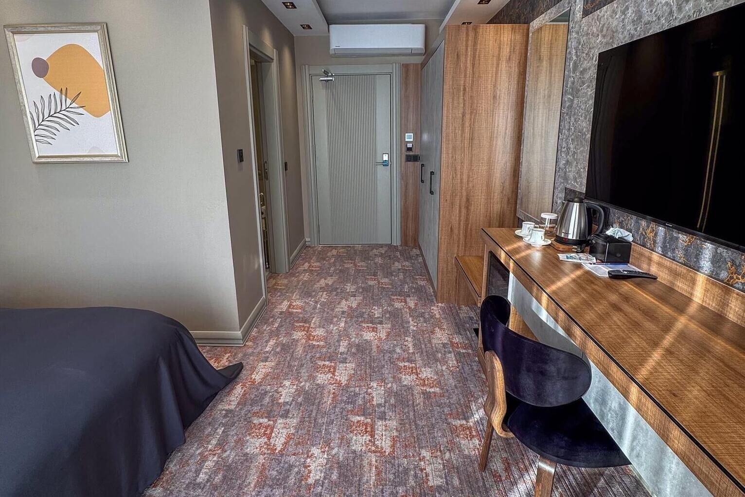 Habitación de hotel con una cama, un escritorio con espejo, cafetera y televisor.