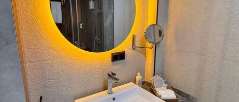A bathroom with a white sink, a mirror with a yellow light, and a shower visible in the background.