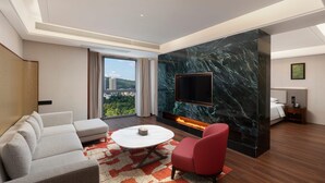 Una camera d'hotel moderna con un divano, una poltrona rossa, una televisione a schermo piatto, un camino e un'ampia finestra con vista sulla città.