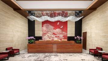 Una recepción con un mural tradicional en rojo y blanco, dos orquídeas en macetas y un candelabro moderno.