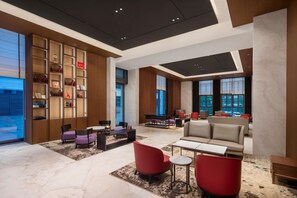 A modern hotel lobby with a large bookshelf, seating area, and large windows.