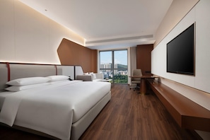 Un cuarto de hotel con una cama grande, un escritorio, un televisor y vistas de la ciudad.