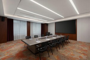 Un salón de conferencias con una larga mesa, sillas, una pantalla de proyector y un amplio ventanal con cortinas.