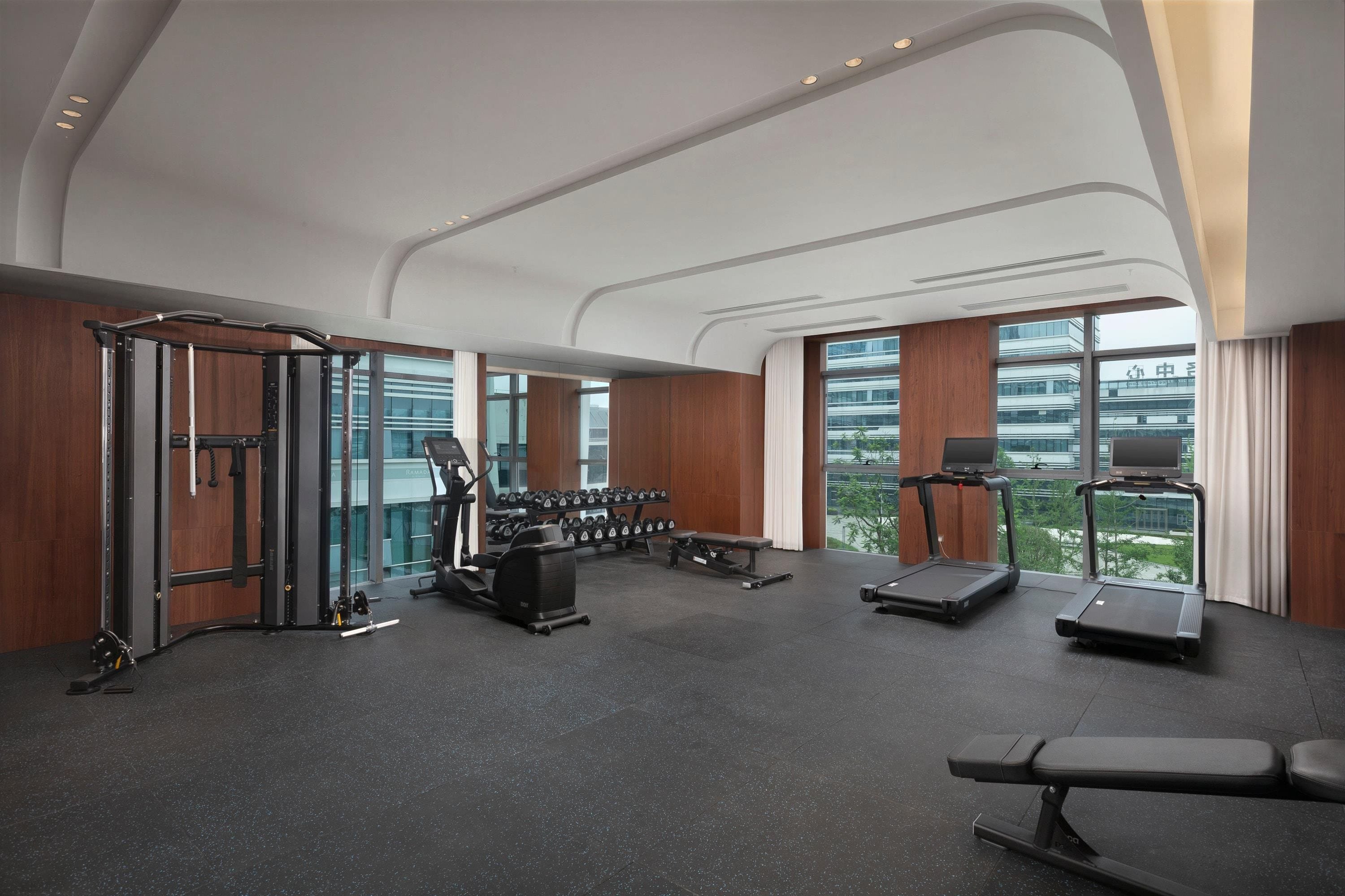 Ett modernt gym med olika typer av träningsutrustning, stora fönster och utsikt över staden.