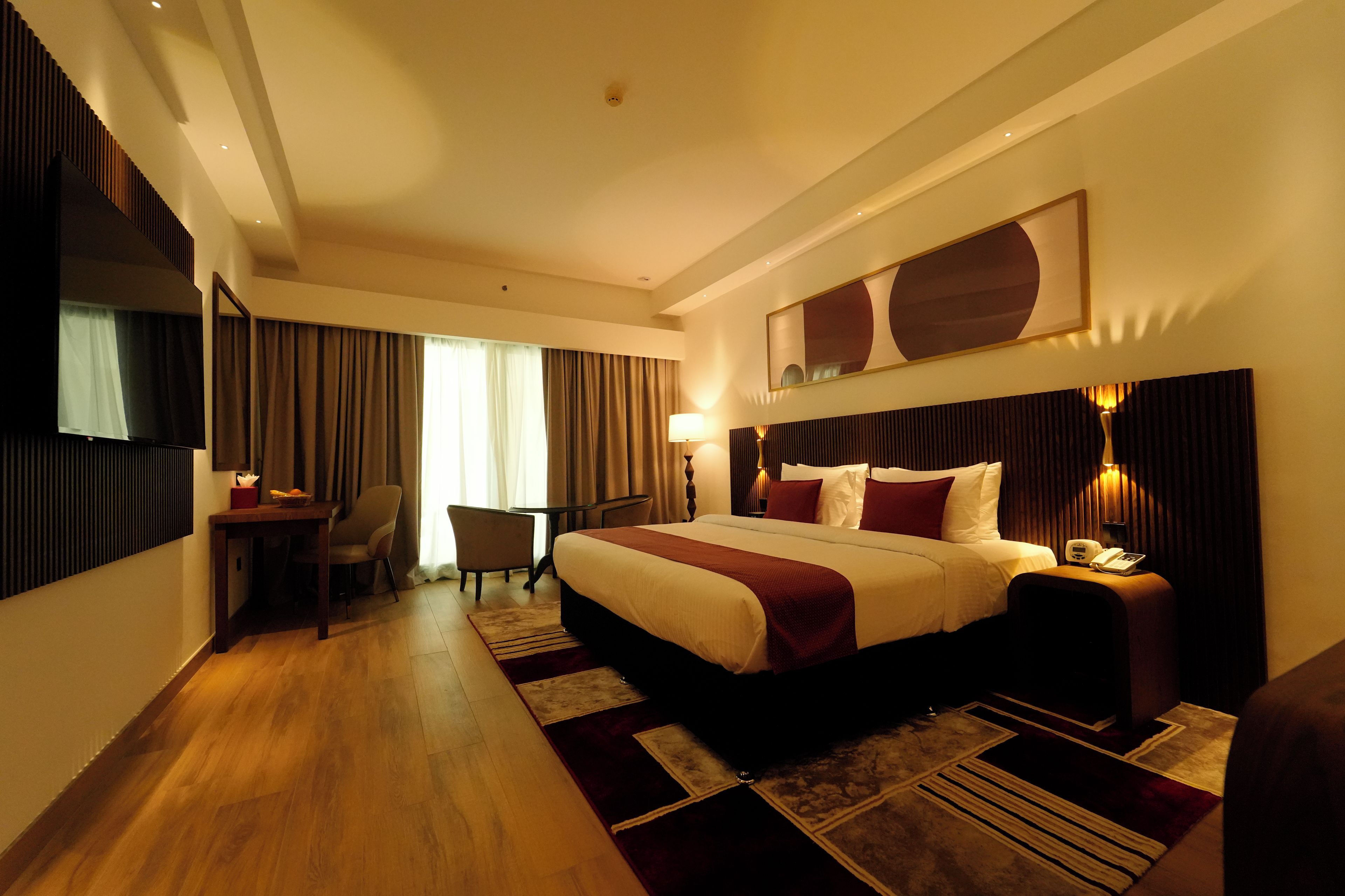 A hotel room with a large bed, a desk, a chair, and a TV.