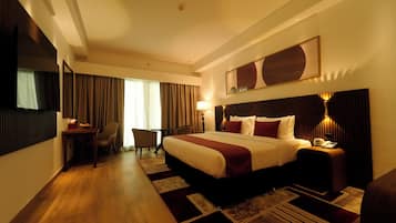 A hotel room with a large bed, a desk, a chair, and a TV.
