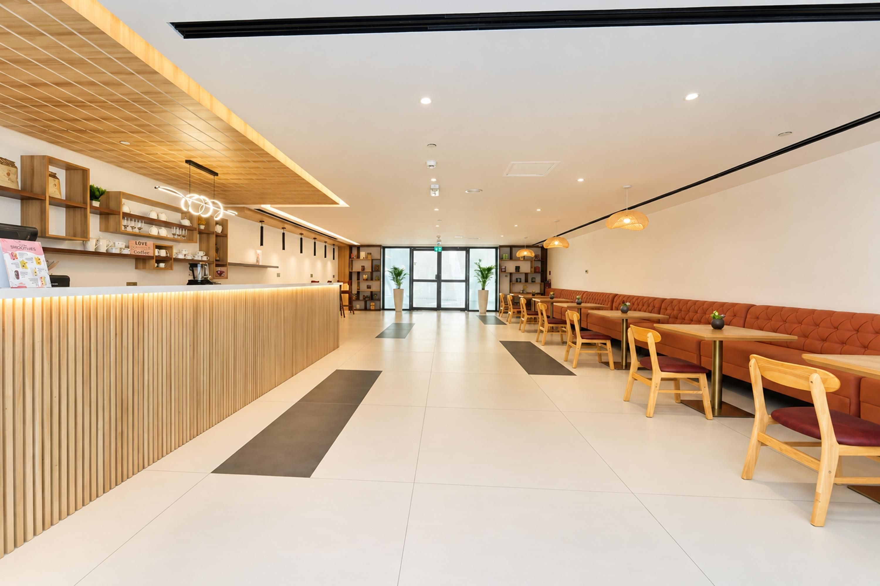 Ein modernes Café-Interieur mit einem Holzbüro, einer Sitzgelegenheit mit Tischen und Stühlen sowie einem großen Fenster, das für natürliches Licht sorgt.
