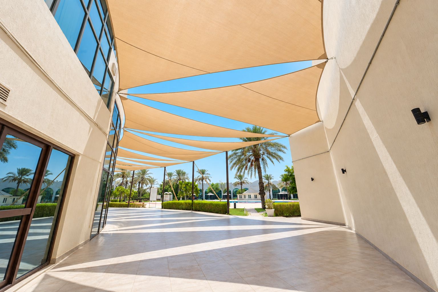A covered walkway with a modern architectural design, featuring a geometric pattern on the floor and a series of beige canopies providing shade.