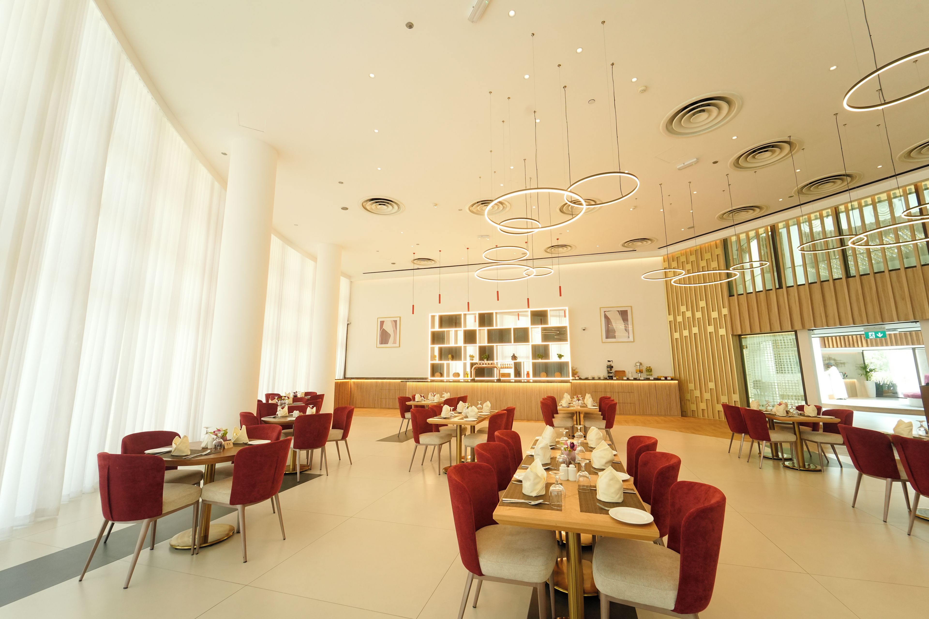 A modern dining area with red chairs, a long table set for a meal, and a contemporary light fixture.