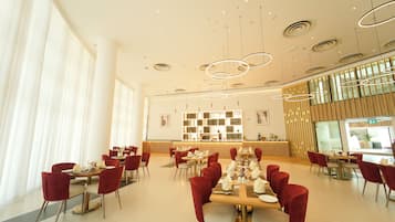 A modern dining area with red chairs, a long table set for a meal, and a contemporary light fixture.