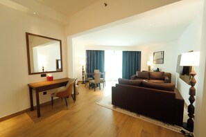 A hotel room with a wooden desk, a brown sofa, a dining area with chairs, and a large mirror on the wall.