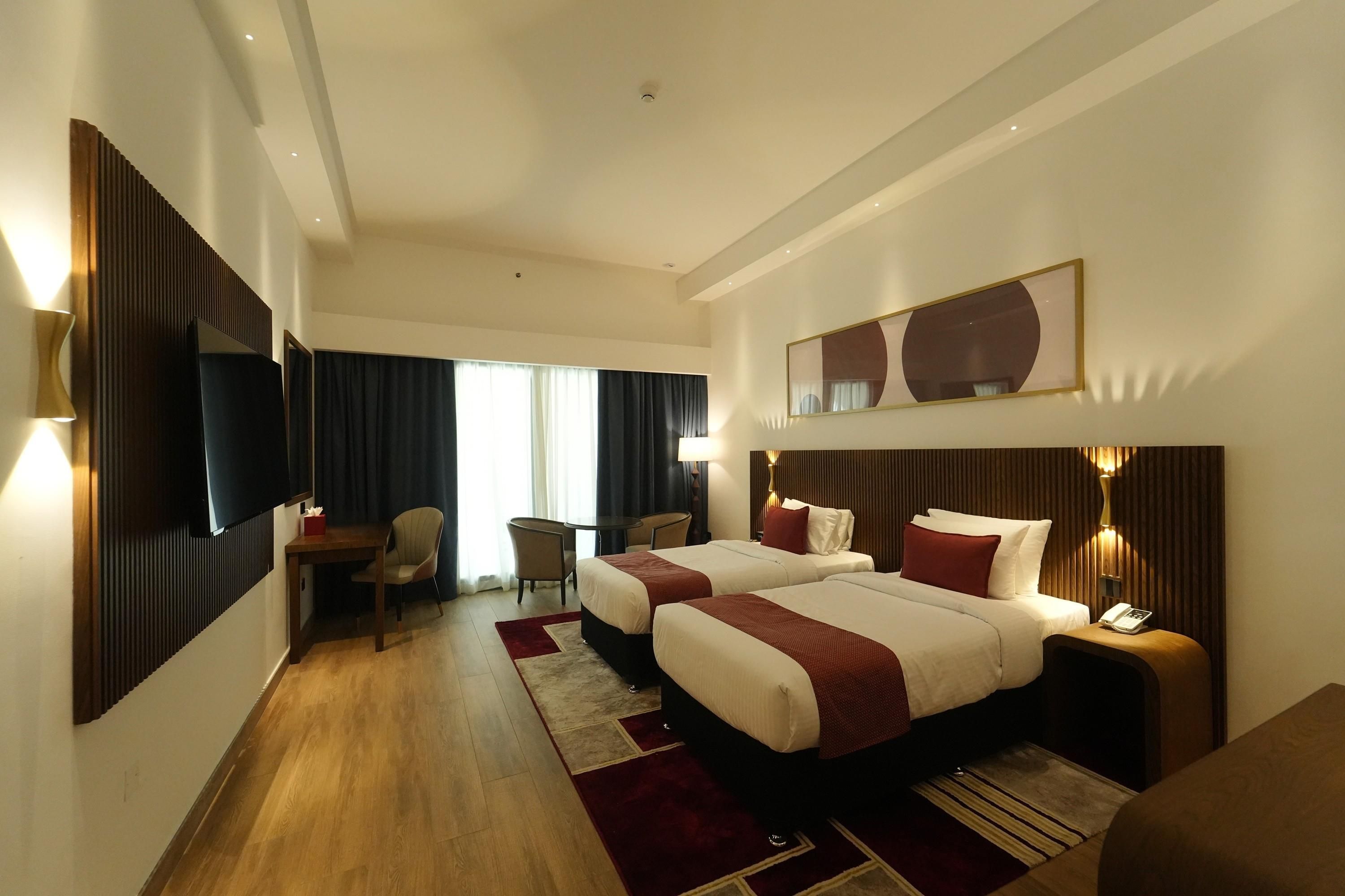 A hotel room with two beds, a desk, a chair, a TV, and a large mirror.