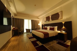 A hotel room with a large bed, a desk, a chair, and a television.