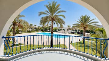 A pool area with a clear blue sky, surrounded by palm trees and a white building with arches.