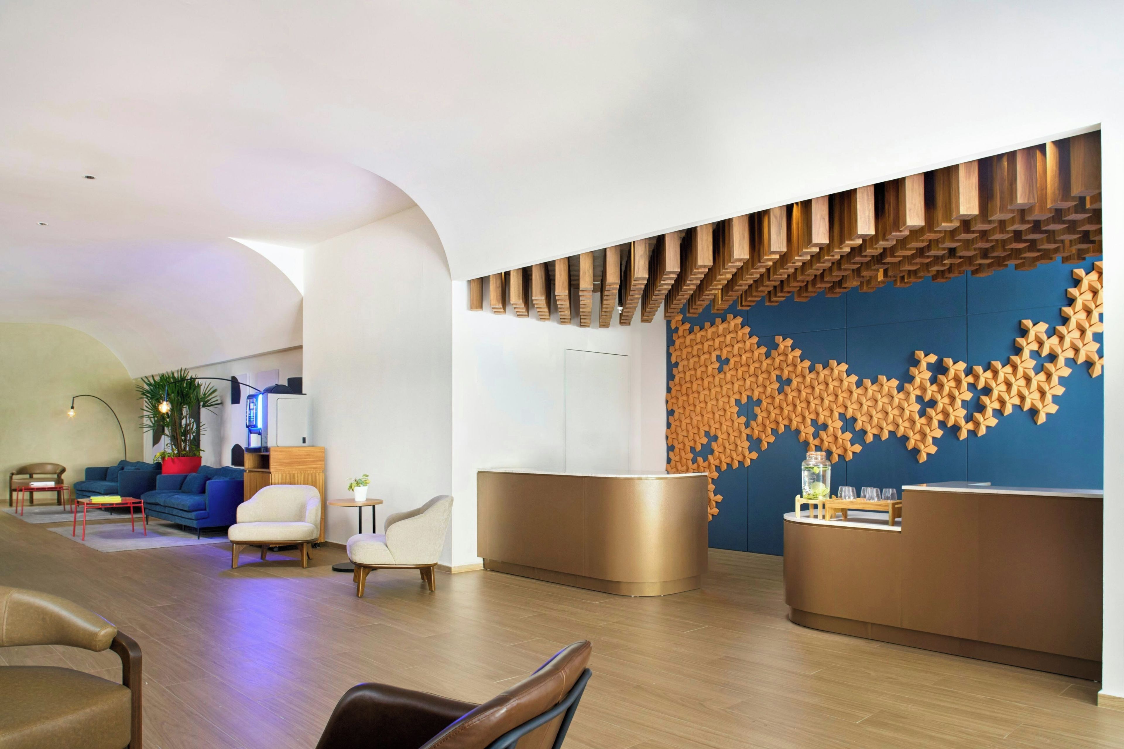A modern reception area with a blue wall and wooden panel design, a seating area with sofas and chairs, and a coffee table.