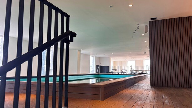 A modern indoor swimming pool with a wooden deck, a black railing, and a ceiling with recessed lighting. - Residence Inn by Marriott Guadalajara Country Club (Guadalajara)