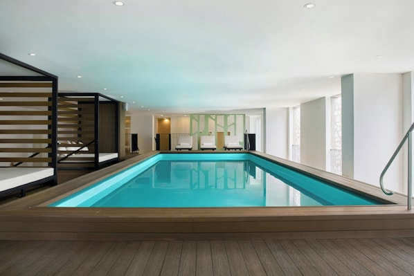 Una piscina interior moderna con un suelo de madera, una escalera con barandilla negra y vista al espacio interior.