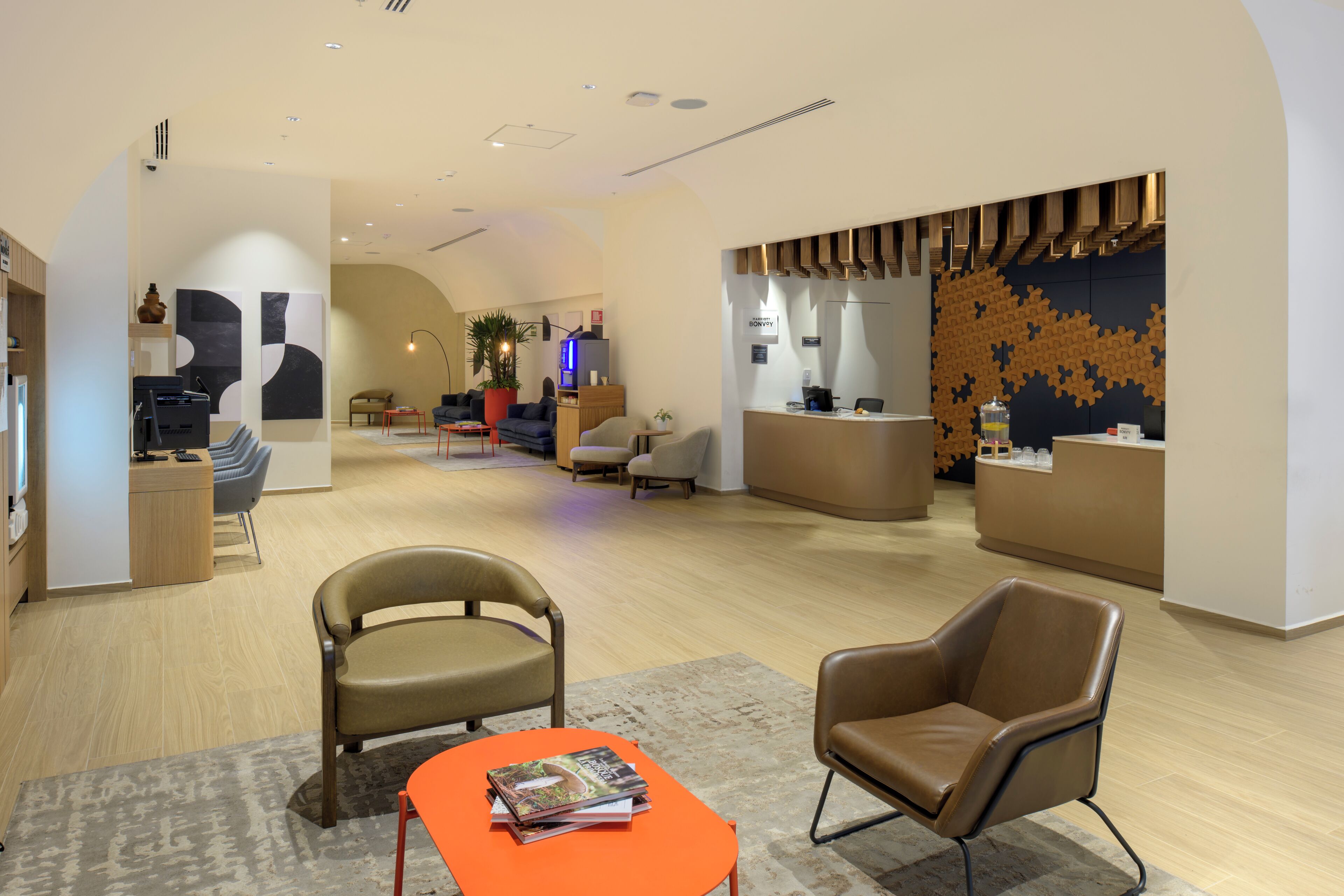 A hotel lobby with a reception desk, seating area, and a large wall mural.