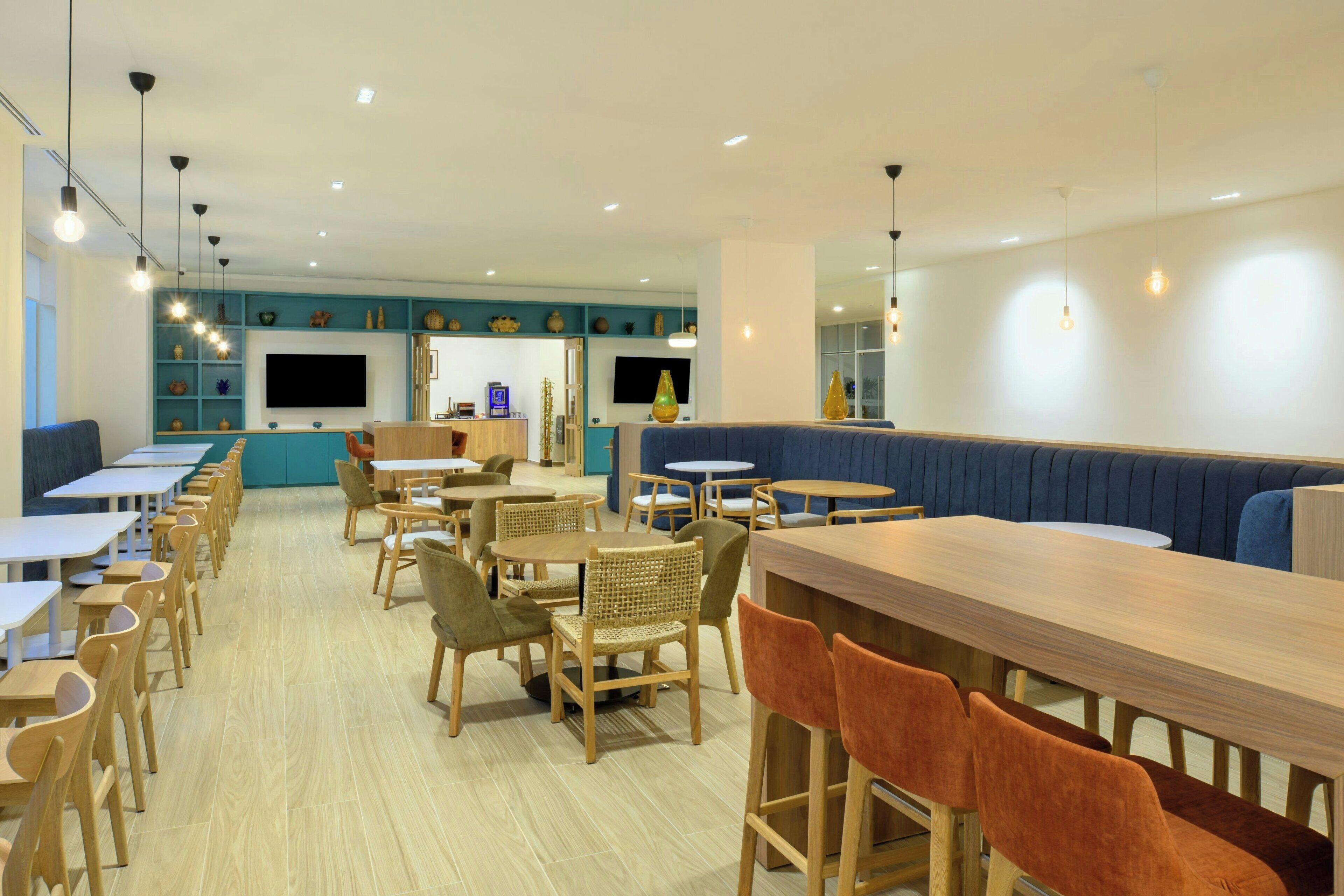 Un interior de restaurante moderno con mesas y sillas de madera, una zona de bar y una sección de estar con sofá.