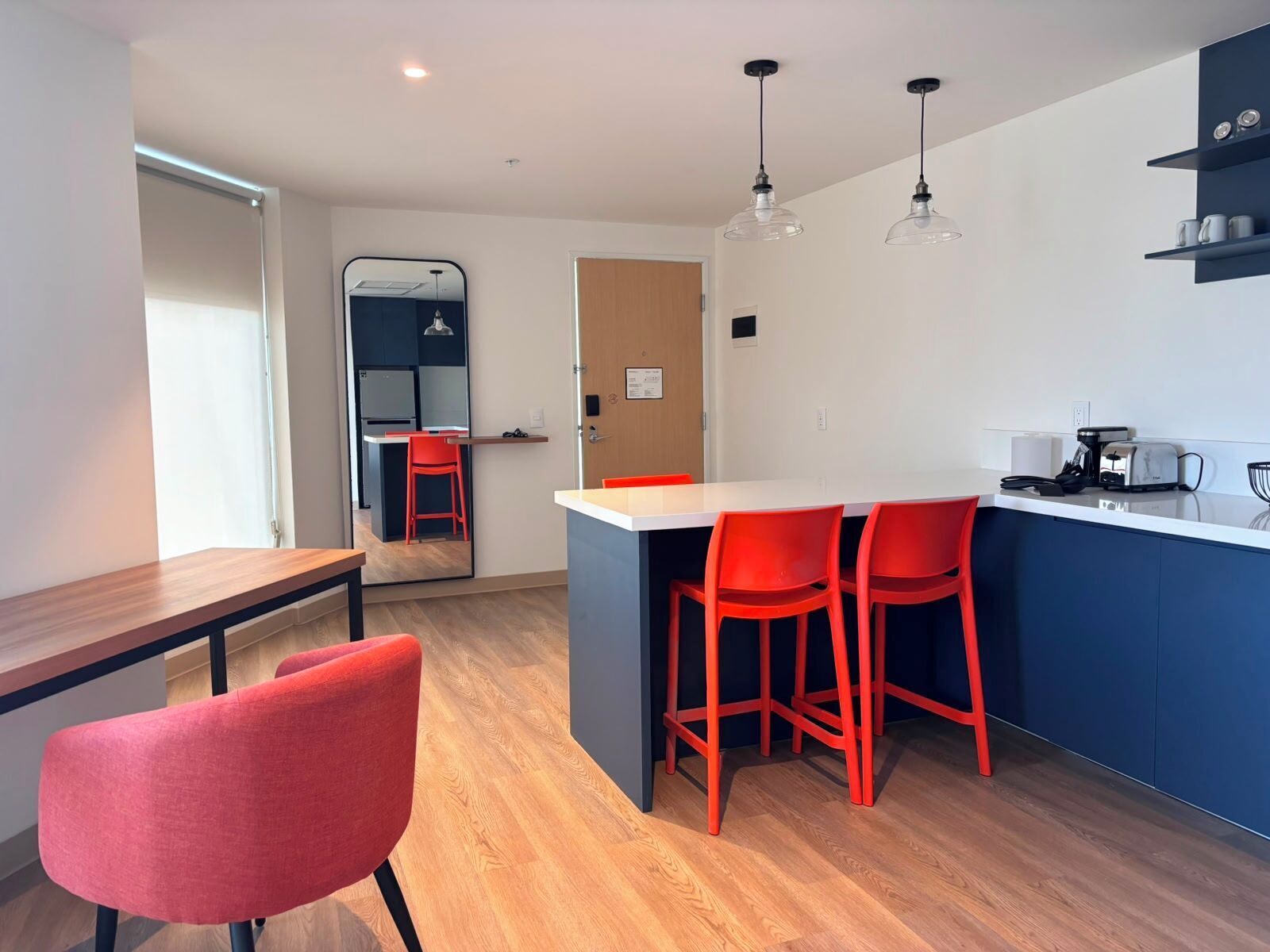 Una cocina moderna con encimera blanca, sillas rojas y un armario azul.