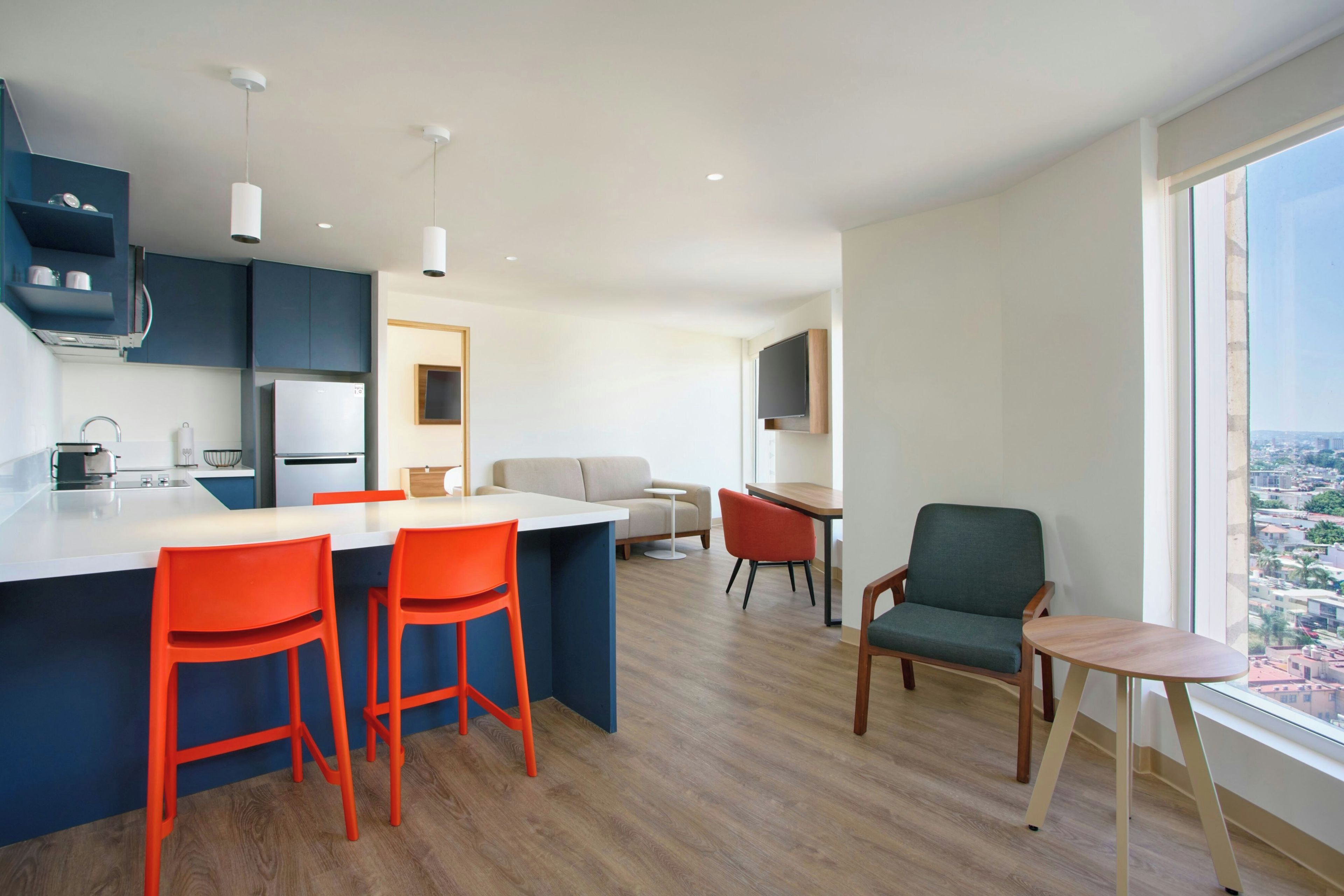 Een moderne keuken met een centraal eiland, een eetgedeelte met tafel en stoelen, en een zithoek met een bank en fauteuils.