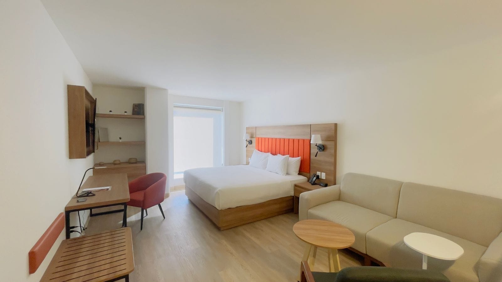 Hotellihuone, jossa on sänky, työpöytä, tuoli, sohva ja pieni pöytä.