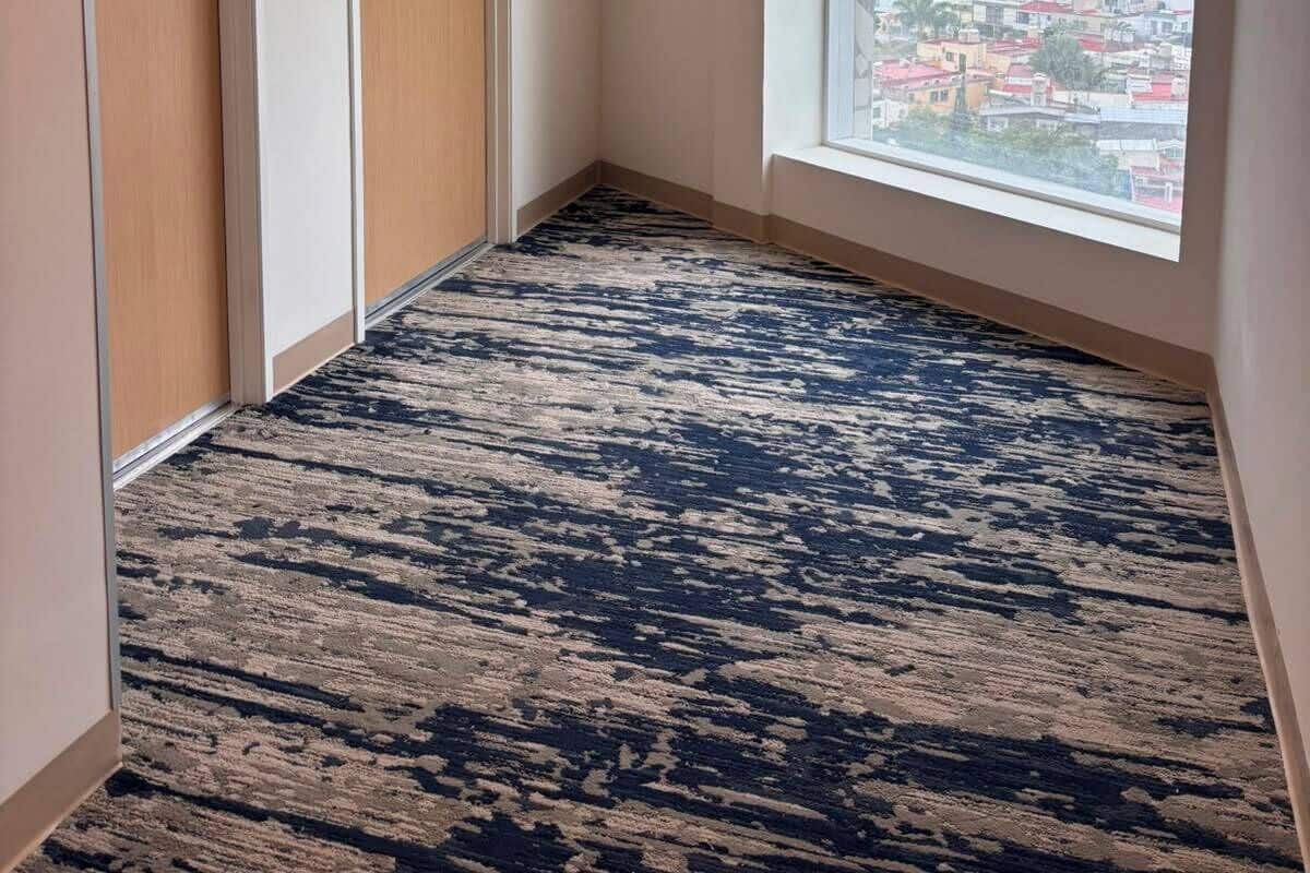 Una habitación de hotel con un ventanal grande, una alfombra estampada y dos puertas.