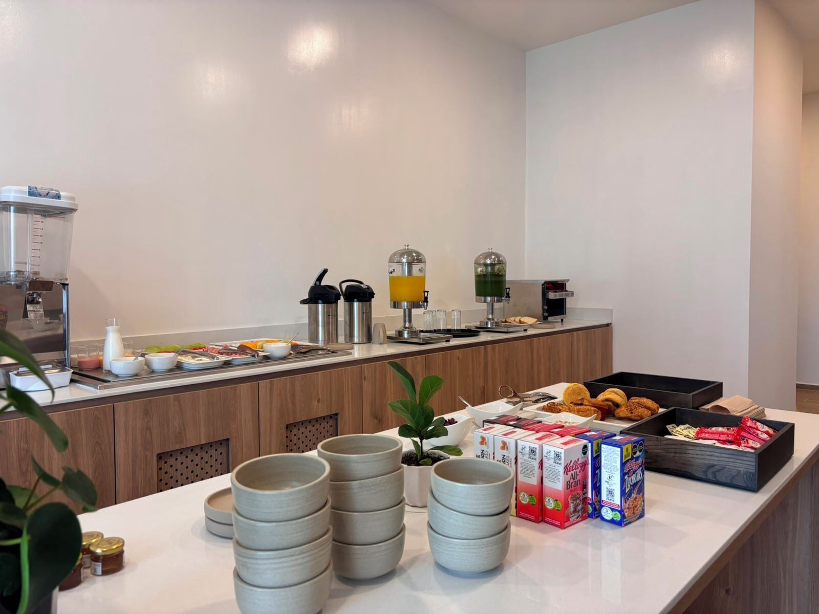 Een ontbijtbuffet met diverse etenswaren, een koffieapparaat en drankdispensers.
