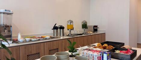Een ontbijtbuffet met diverse etenswaren, een koffieapparaat en drankdispensers.