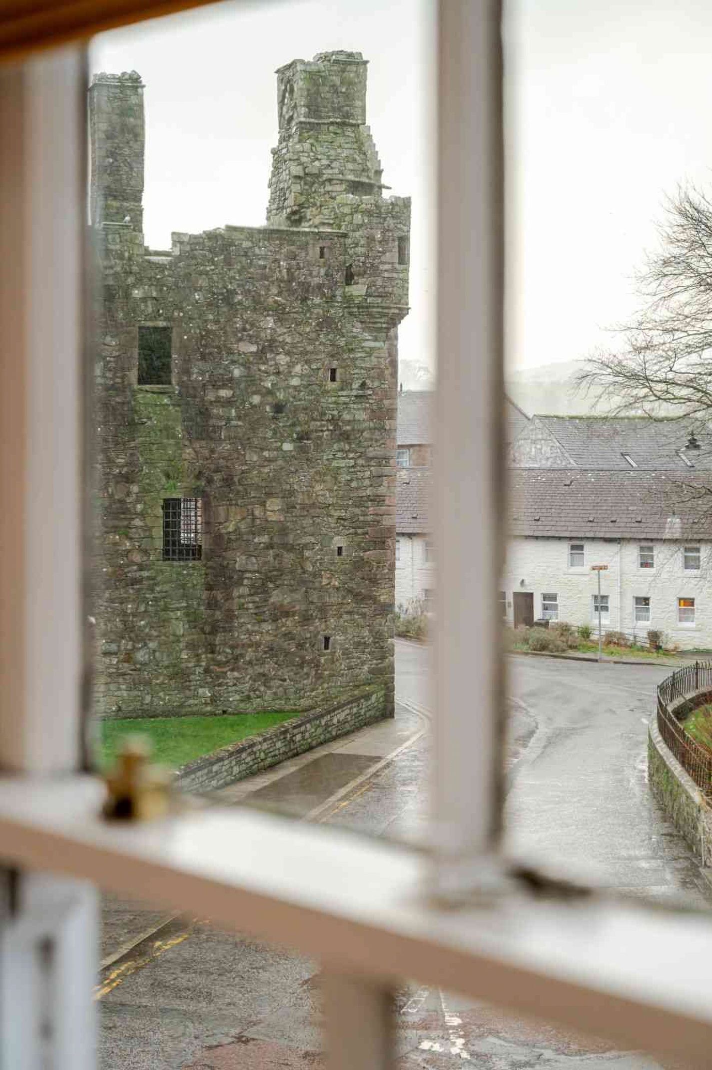 A stone building with a window, a paved road, and a white building in the background.