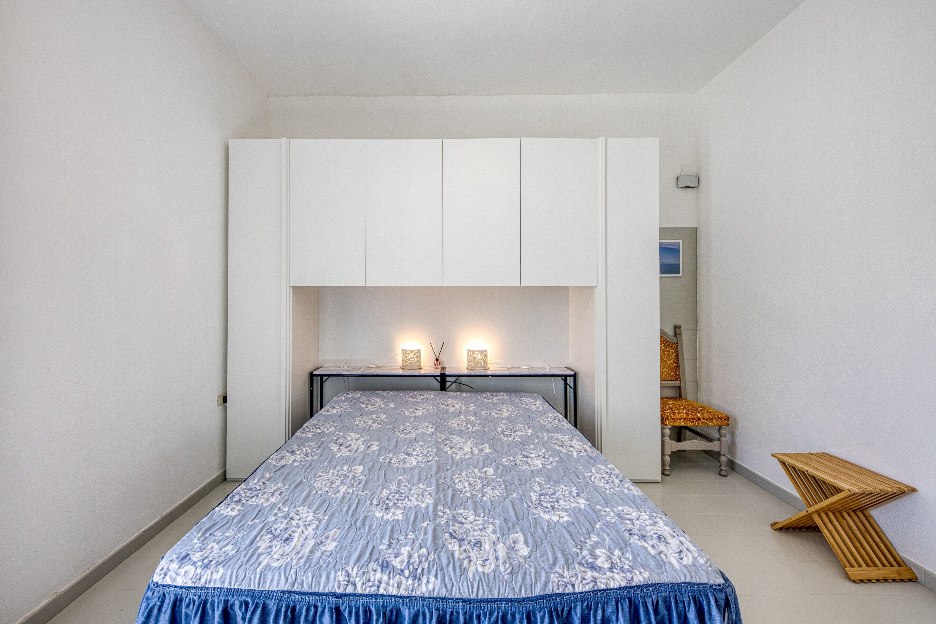 Un dormitorio con cama, armario blanco, lámparas de noche y una silla.