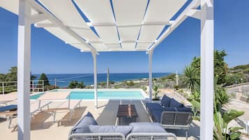 Un espacio exterior techado con piscina, sillas de descanso y vistas al mar.