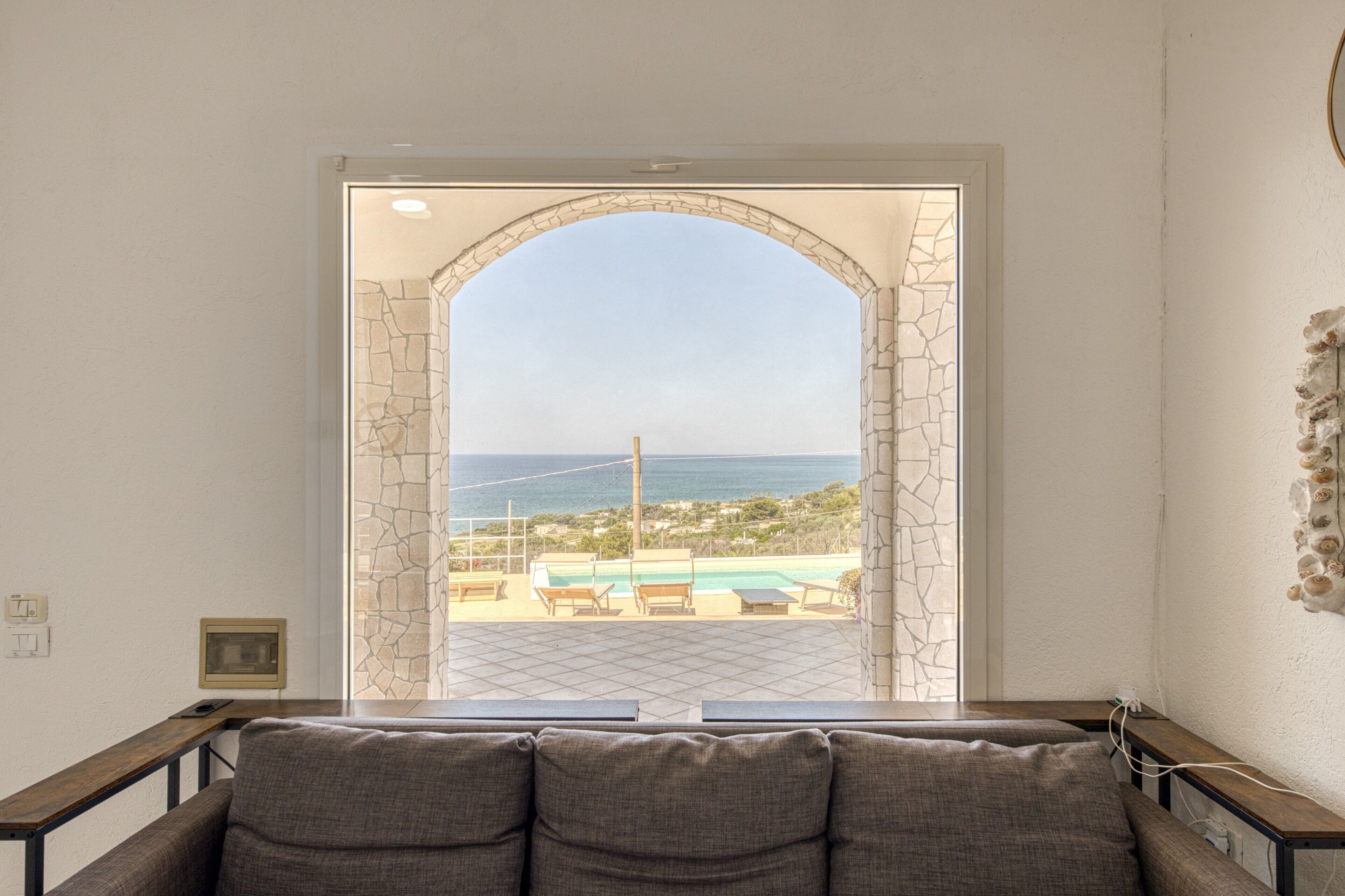 Una habitación con vista a una piscina y al mar, un arco de piedra y un sofá.